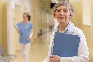 Senior doctor standing in hospital hallway holdings patient files