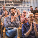 Large group of happy participants applauding on a seminar in a meeting room.