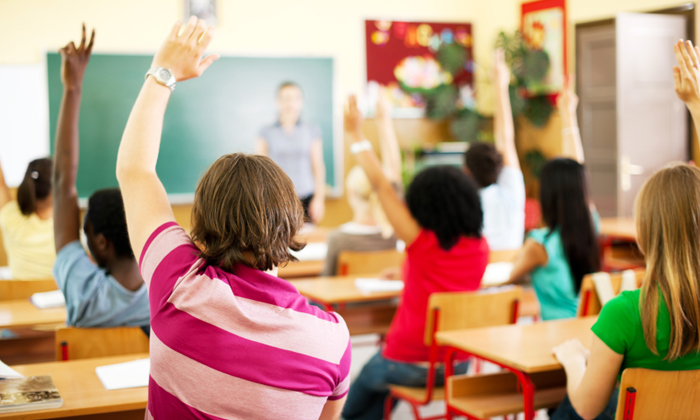 Classroom with happy teenagers raising their hands.